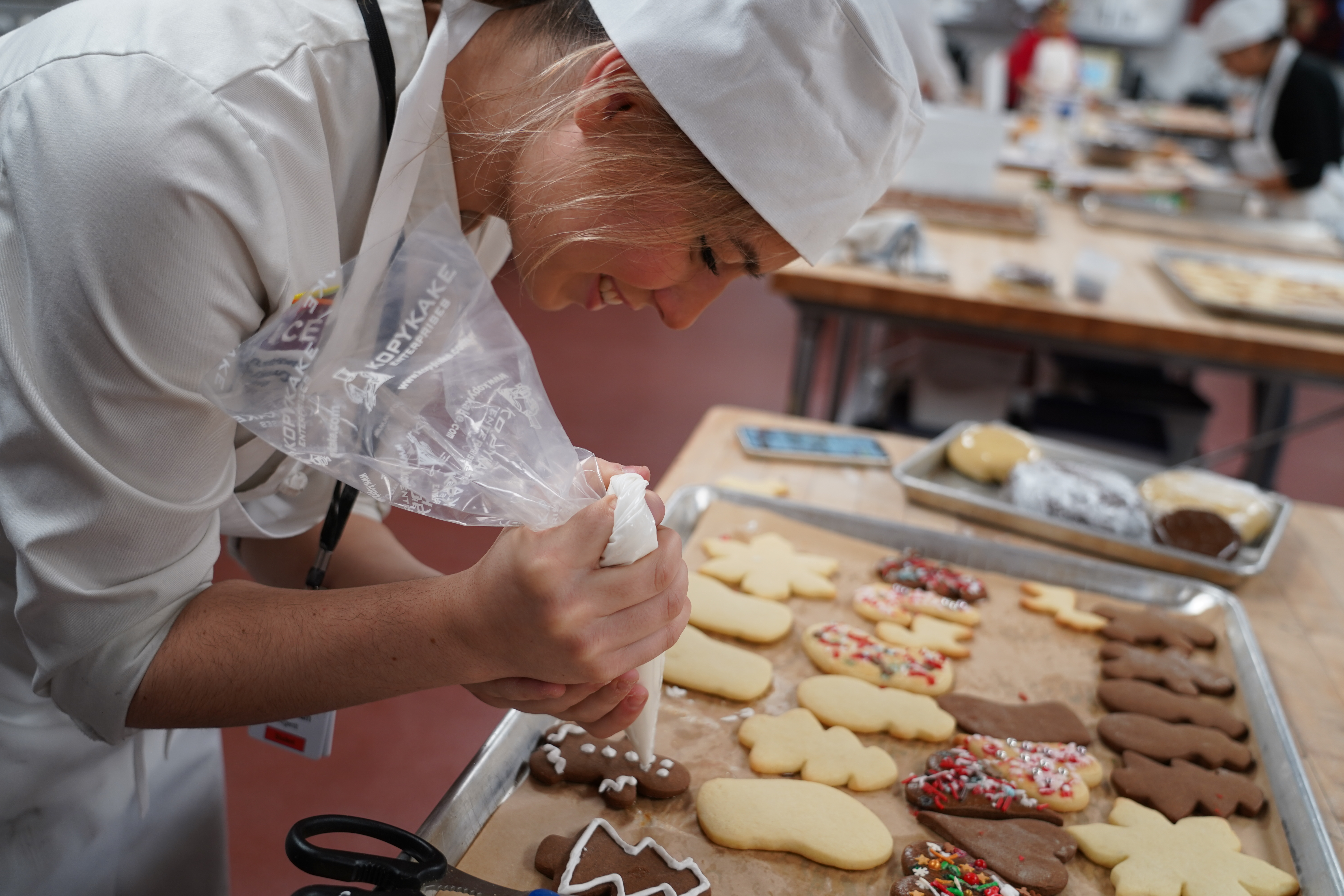 A student pipes royal icing onto gingerbread cookies