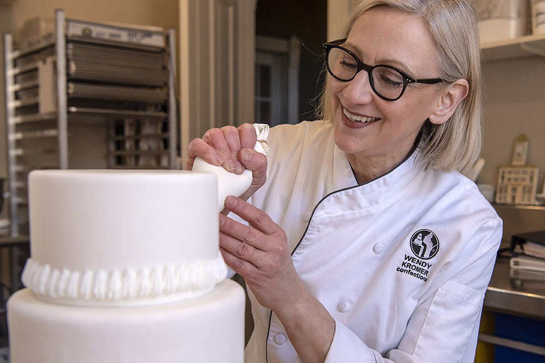 Wendy Kromer pipes icing on a cake in her home.