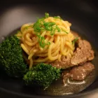 A dish of egg noodles with beef and broccoli sits in a black bowl