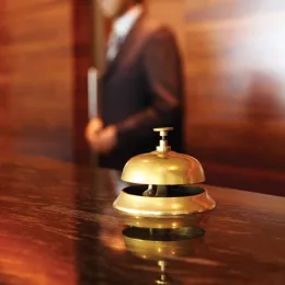 Hotel bell on the front desk of a hotel lobby with a front desk receptionist in the background