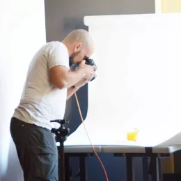 A man takes a photo of a cocktail on a white backdrop during a food photo shoot