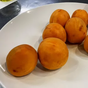 Seven whole apricots sit on a white plate