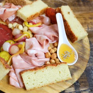 Assorted charcuterie meats, vegetables and bread sit on a brown board