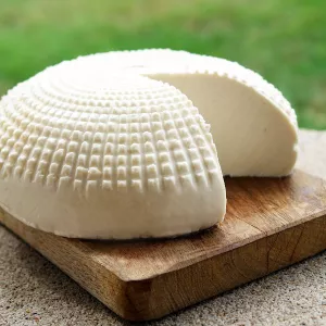 A wheel of goat cheese with a piece cut out sits on a wooden board