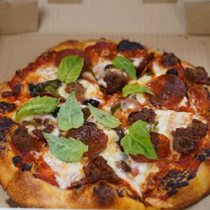 A pizza with cheese, pepperoni, basil and sausage sits in a brown cardboard box