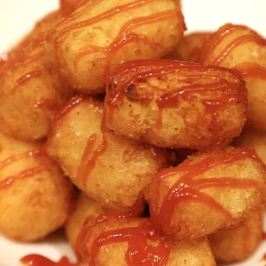 Tater tots with ketchup on top sit on a white plate