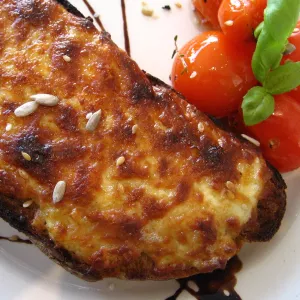 Cheesy toasted welsh rarebit sits on a white plate next to small tomatoes