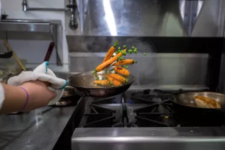 Culinary school student flips a saute pan full of carrots and peas