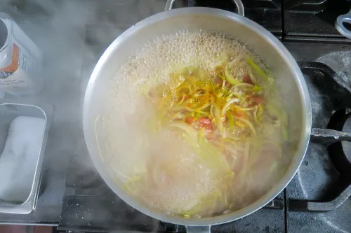 A pot of stock and soup and noodles simmers away on a stove at culinary school