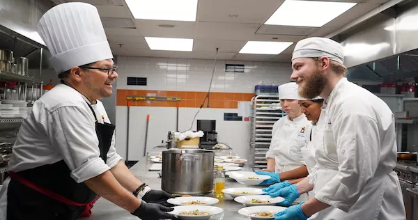 A Plant-Based Culinary Arts student and Chef-Instructor serve a plated dish together