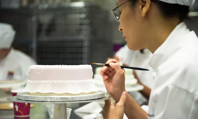 An ICE cake decorating student brushes a cake to make a flower decoration in class