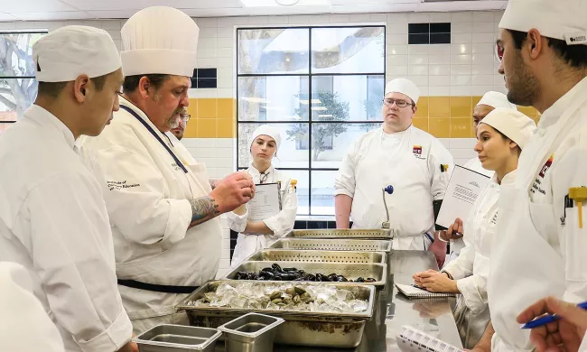 Culinary school students in class as an ICE chef instructor demonstrates a technique
