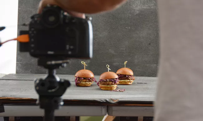 A food photographer sets up a shot of three hamburgers on a photo surface