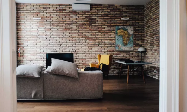 A grey couch in an apartment with brick walls, photo by Justin Schuler via Unsplash