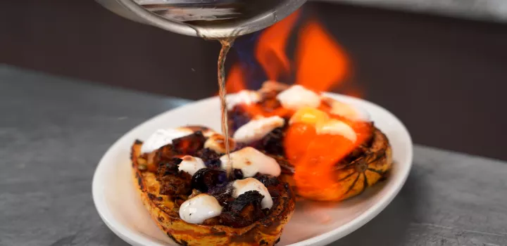 A pot of flaming liquid pours onto a stuffed squash on a white plate