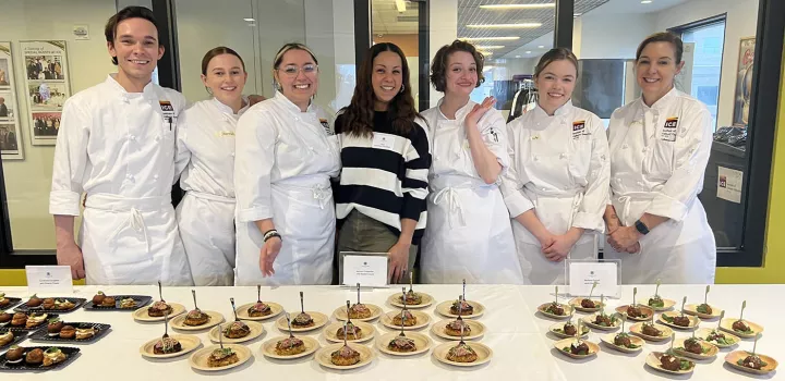 Chef Adrienne Cheatham stands with a group of ICE students behind a table of small plated dishes