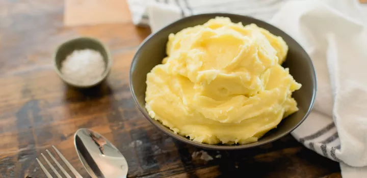 A bowl of mashed potatoes is served with salt on the side.