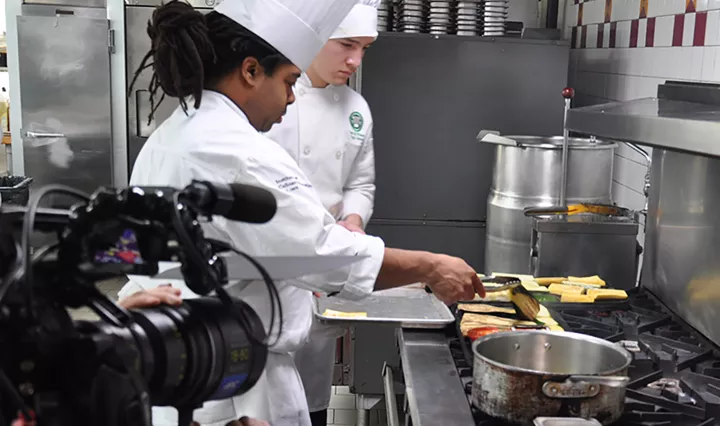 A culinary student cooks vegetables on camera.