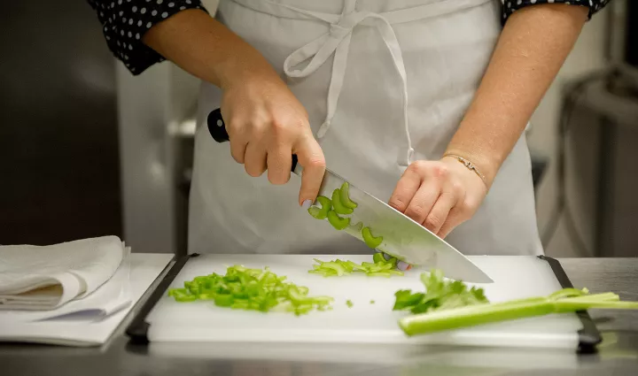 A culinary student uses a knife to chop celery.